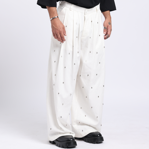Man wearing a black sweater with a white design and white pants on a white background