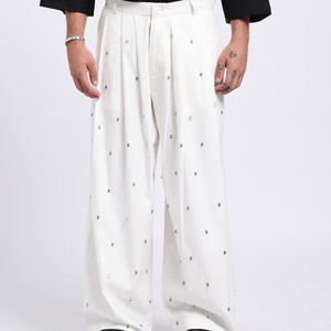 Person wearing a black oversized t-shirt with a white design and white pants with black dots on a white background